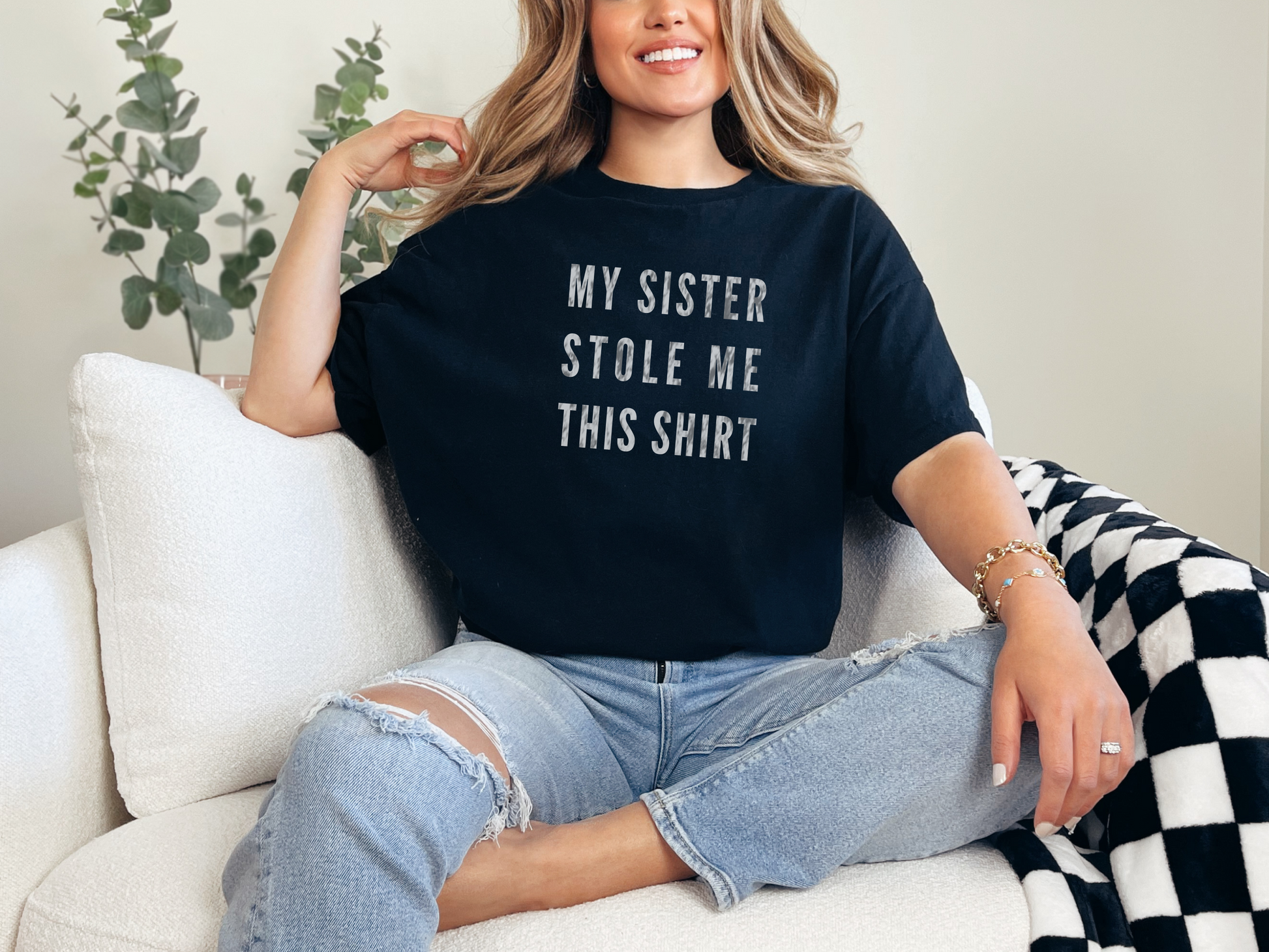 a woman sitting on a couch wearing a black shirt that says, my sister stole