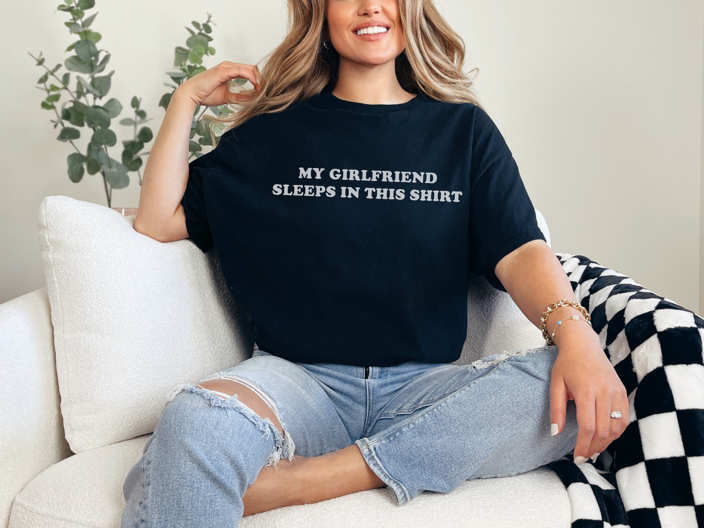 a woman sitting on a couch wearing a black shirt that says my girlfriend sleeps in