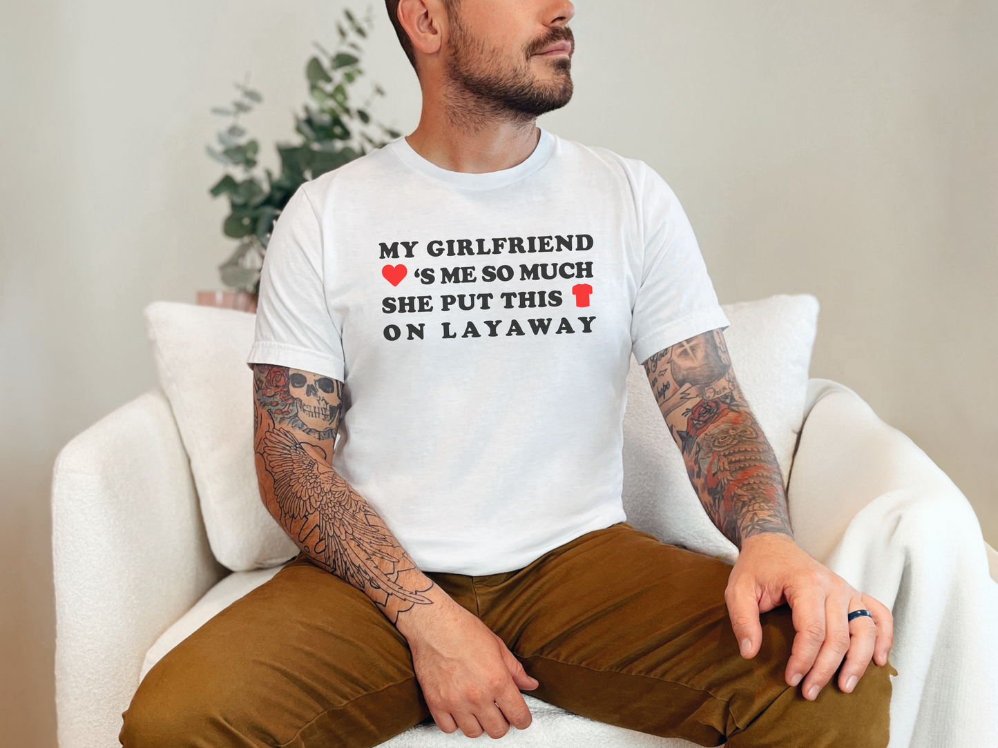 a man sitting on a white couch wearing a t - shirt that says my girlfriend