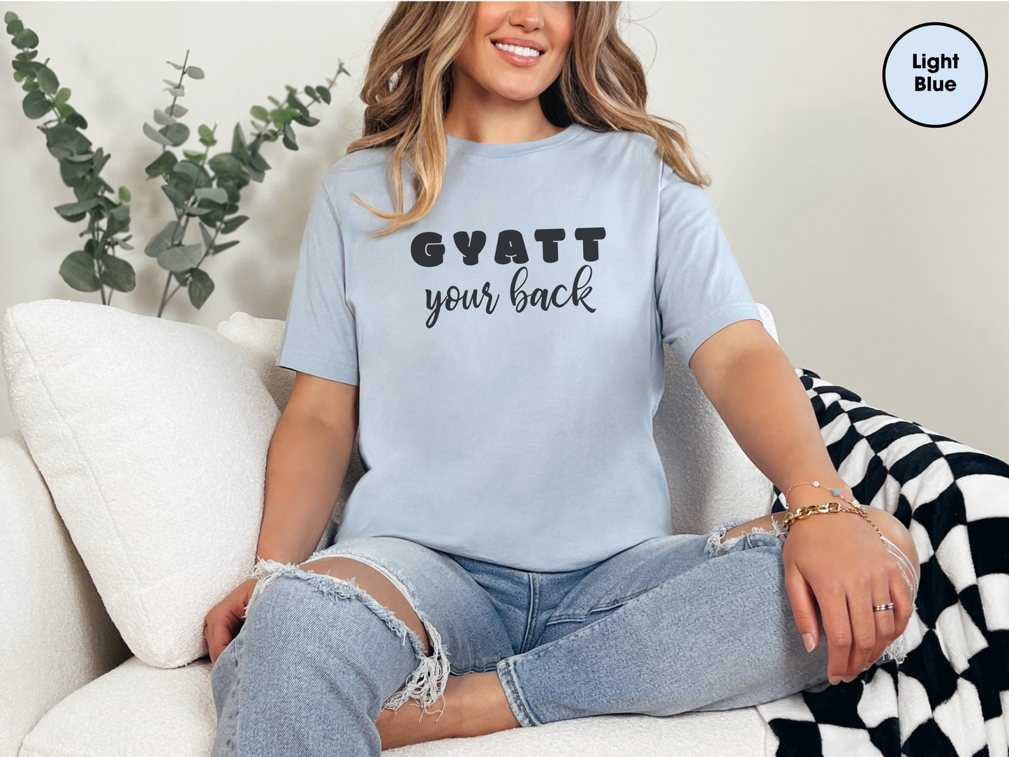 a woman sitting on a couch wearing a blue shirt that says gyatt your